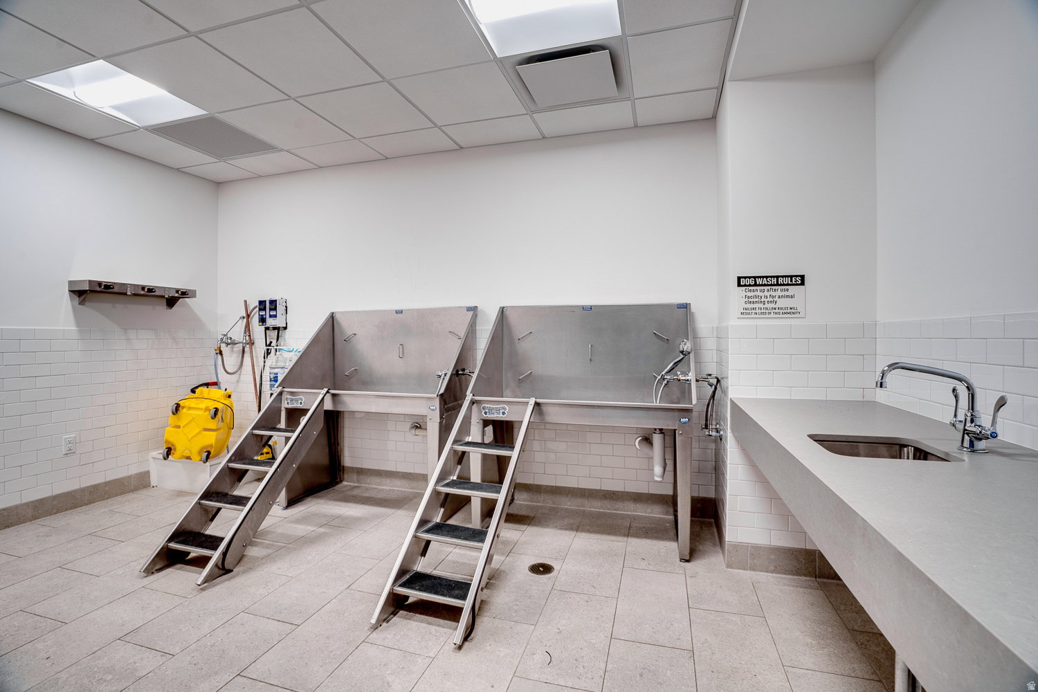 Misc room with a drop ceiling, a wainscoted wall, pet washing station, and tile walls