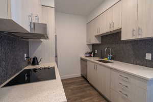 Kitchen featuring dark wood-style floors, light stone countertops, black electric cooktop, dishwasher, and light wood finish cabinetry