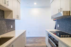 Kitchen featuring backsplash, light stone countertops, stainless steel oven, and recessed lighting