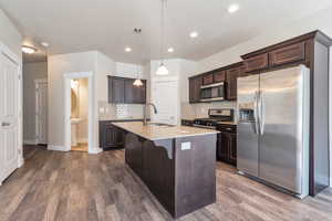Kitchen featuring stainless steel appliances, light stone counters, dark wood finish cabinets, a breakfast bar, and decorative light fixtures