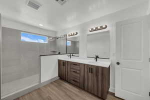 Bathroom featuring light wood-style floors, double vanity, a walk in shower, and a textured ceiling