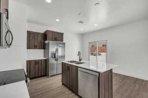 Kitchen featuring dark wood finish cabinets, stainless steel appliances, a kitchen island with sink, light wood-style flooring, and a textured ceiling