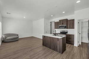 Kitchen featuring stainless steel appliances, dark wood finish cabinets, a center island with sink, dark wood-style floors, and a kitchen breakfast bar