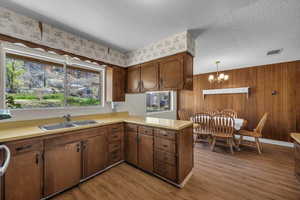 Kitchen featuring light countertops, a peninsula, suspended lighting, wooden walls, and dark wood-style flooring