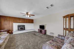 Carpeted living area featuring ceiling fan, a wood stove, wooden walls, and a textured ceiling