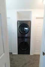 Laundry area with stacked washer and clothes dryer and dark carpet
