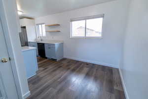 Kitchen featuring light countertops, dark wood-type flooring, open shelves, black dishwasher, and freestanding refrigerator