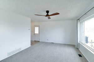 Spare room with a ceiling fan, a textured ceiling, and light carpet