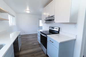 Kitchen with stainless steel electric stove, white cabinetry, dark wood-type flooring, black dishwasher, and open shelves