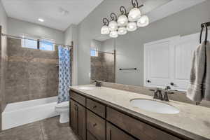Bathroom featuring double vanity, shower / bathtub combination with curtain, and dark tile patterned floors