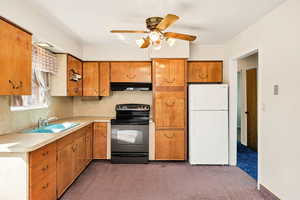 Kitchen featuring black / electric stove, freestanding refrigerator, light countertops, ceiling fan, and dark colored carpet