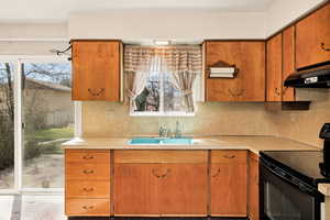 Kitchen with black range with electric stovetop, wood finish cabinetry, light countertops, and backsplash