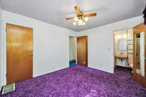 Unfurnished bedroom with dark carpet, a ceiling fan, and connected bathroom