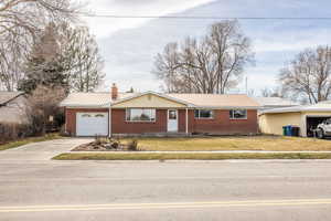 Single story home with a metal roof, a chimney, a front yard, a garage, and brick siding