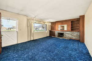Unfurnished living room featuring dark carpet, a stone fireplace, and built in features