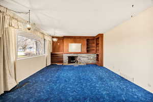Unfurnished living room featuring built in shelves, carpet, and a stone fireplace