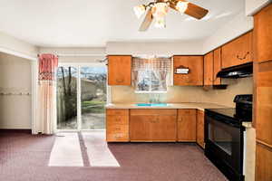 Kitchen featuring black range with electric cooktop, light countertops, dark carpet, decorative backsplash, and wood finish cabinetry