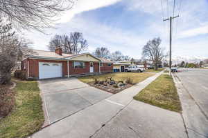 Ranch-style home with driveway, brick siding, a chimney, a garage, and a front yard