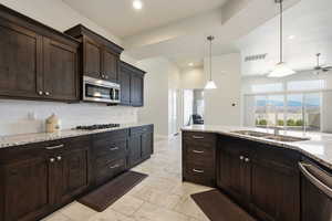 Kitchen with light stone counters, dark wood finish cabinetry, hanging light fixtures, stainless steel appliances, and a ceiling fan