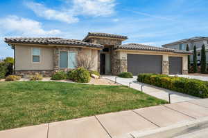 Prairie-style house with stone siding, a garage, a front yard, driveway, and stucco siding