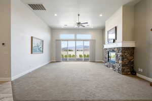 Unfurnished living room with ceiling fan, light colored carpet, a fireplace, a mountain view, and a high ceiling