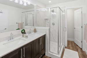 Bathroom with double vanity, a marble finish shower, and dark wood-type flooring