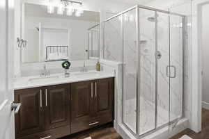 Ensuite bathroom featuring double vanity, a marble finish shower, and dark wood-style flooring