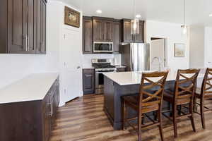Kitchen with dark wood finish cabinetry, stainless steel appliances, dark wood-style floors, a kitchen breakfast bar, and an island with sink