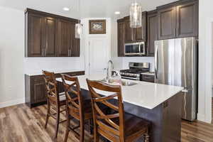 Kitchen featuring dark wood finish cabinets, stainless steel appliances, an island with sink, and pendant lighting