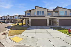 Contemporary house with a garage, stone siding, concrete driveway, and a front yard