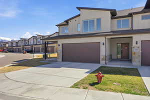 View of front facade featuring stone siding, a garage, driveway, board and batten siding, and a front lawn