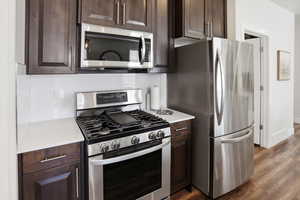 Kitchen with stainless steel appliances, dark wood finish cabinetry, and dark wood-style floors