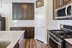 Kitchen featuring stainless steel appliances, dark wood finish cabinetry, dark wood finished floors, light stone countertops, and tasteful backsplash