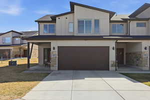 View of front facade featuring stone siding, a garage, stucco siding, and a front lawn