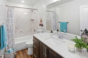Full bath featuring vanity, shower / bathtub combination with curtain, and dark wood finished floors
