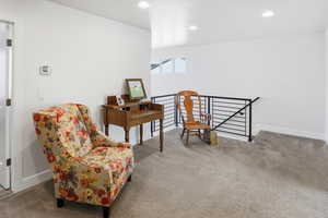 Living area with light colored carpet, recessed lighting, and an upstairs landing