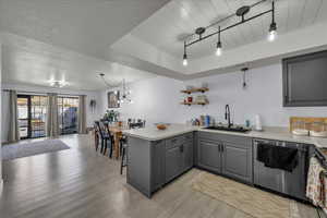 Kitchen featuring gray cabinetry, a peninsula, dishwasher, light countertops, and light wood finished floors