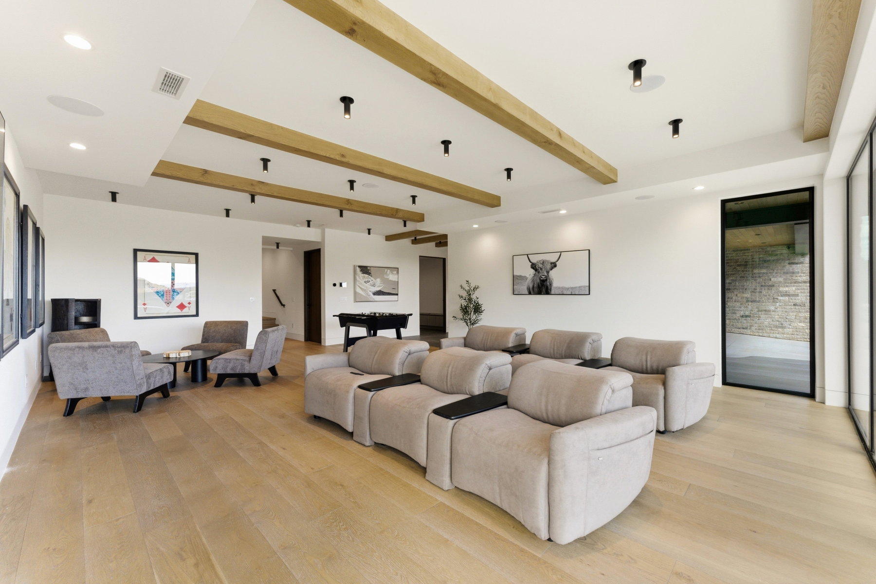 Spacious entertainment room featuring wood-finish flooring, exposed ceiling beams, recessed lighting, and large format windows