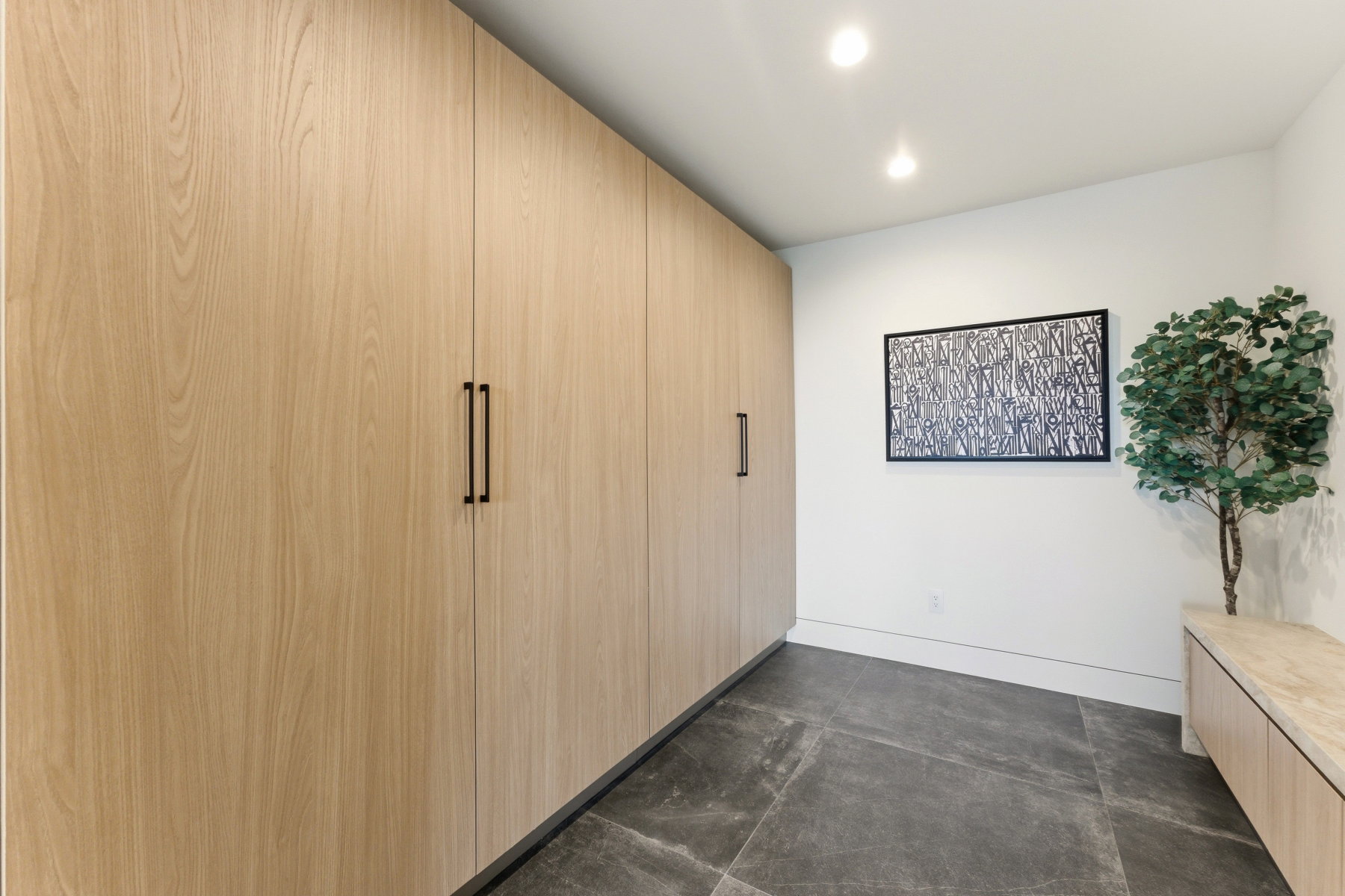 Integrated wood-finish cabinetry featuring matte black hardware, recessed lighting, and large format grey tile flooring