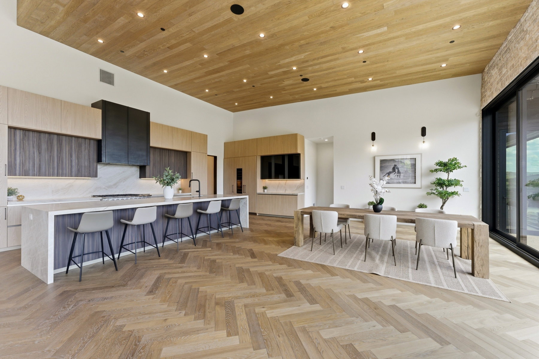 Open-concept kitchen and dining area featuring herringbone wood-finish flooring, a large kitchen island with seating, integrated appliances, and a wood-paneled ceiling with recessed lighting