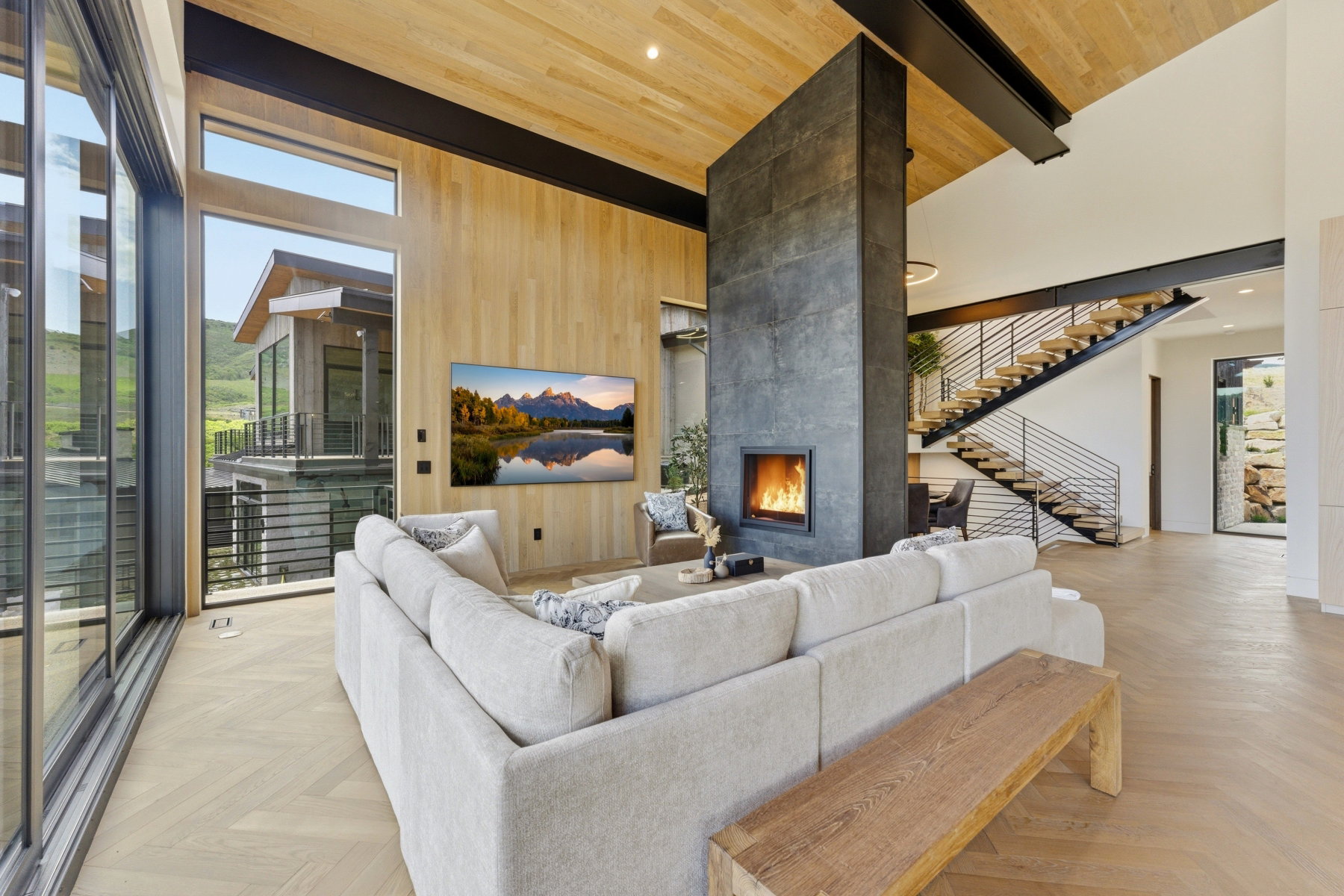 Expansive living area featuring large format glass sliding doors, a floor-to-ceiling stone fireplace, a floating staircase with modern metal railings, and wood-finish flooring