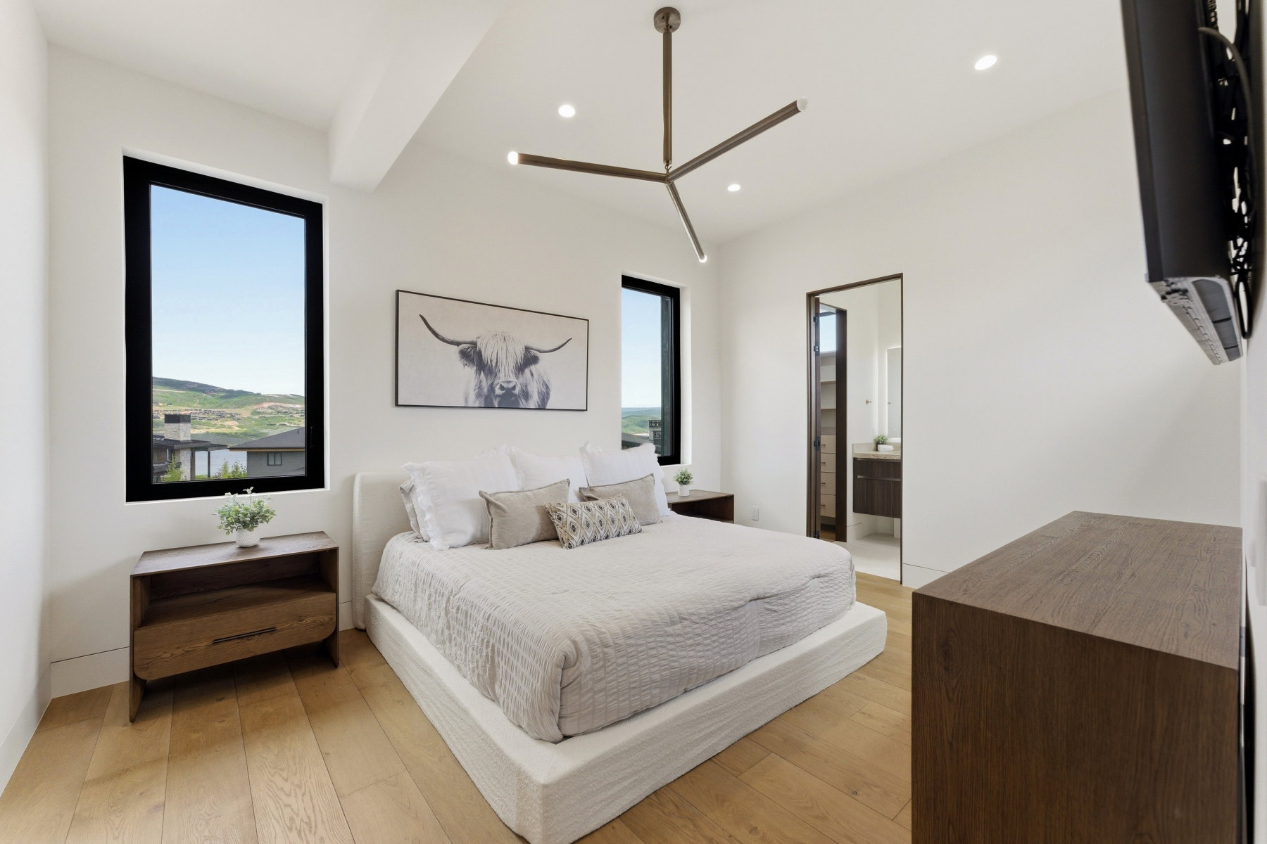 Bright room featuring expansive windows with black frames, offering clear mountain and distant residential scenery