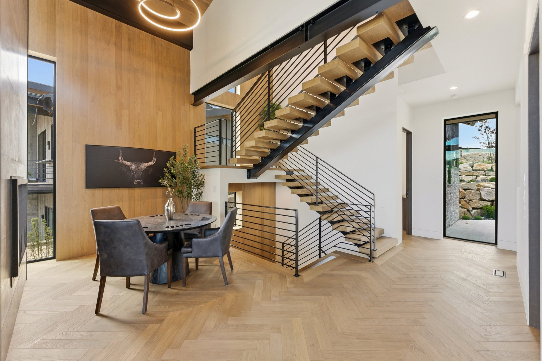 Soaring ceilings with a contemporary chandelier, herringbone wood-finish flooring, and a floating staircase with sleek metal railings