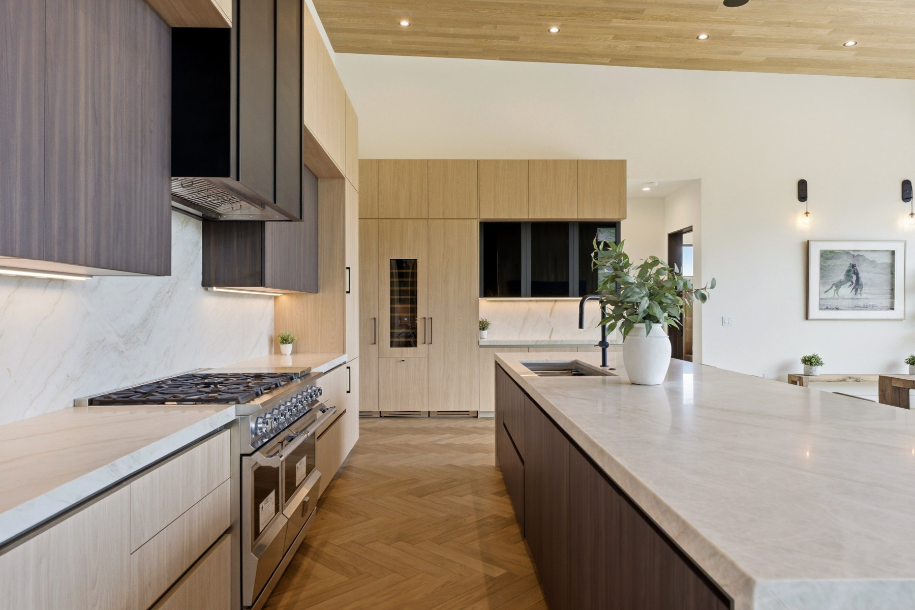 Gourmet kitchen featuring a substantial island with an undermount sink, a professional-grade gas range, a paneled refrigerator, a built-in wine cooler, and herringbone wood-finish flooring
