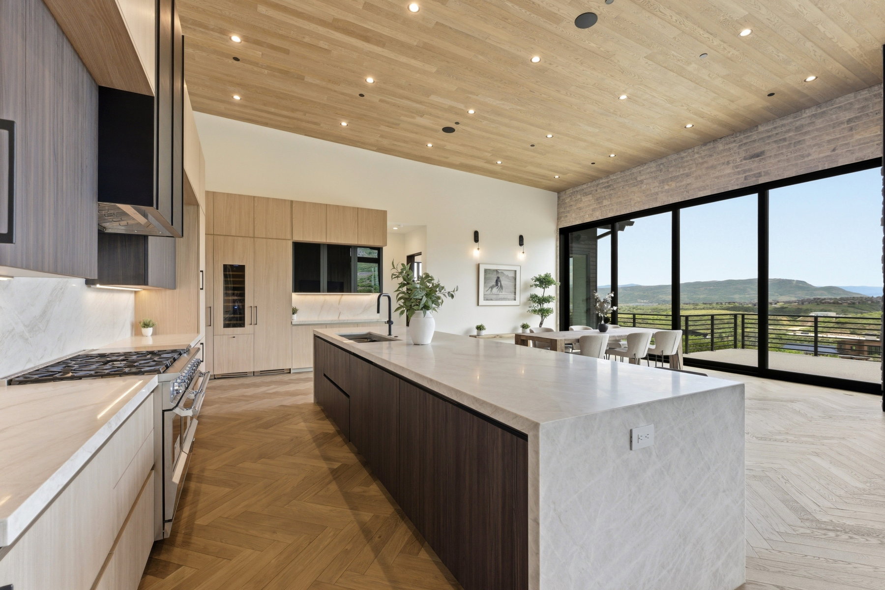 Open-concept kitchen featuring wood-finish herringbone flooring, a large island with stone countertop, integrated appliances, and extensive cabinetry