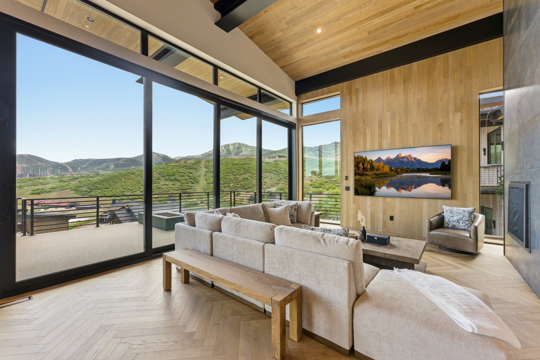 Spacious living area featuring expansive floor-to-ceiling windows, wood-finish flooring in a herringbone pattern, a vaulted wood-paneled ceiling, a wood-slat accent wall, and a built-in fireplace with a stone-finish surround
