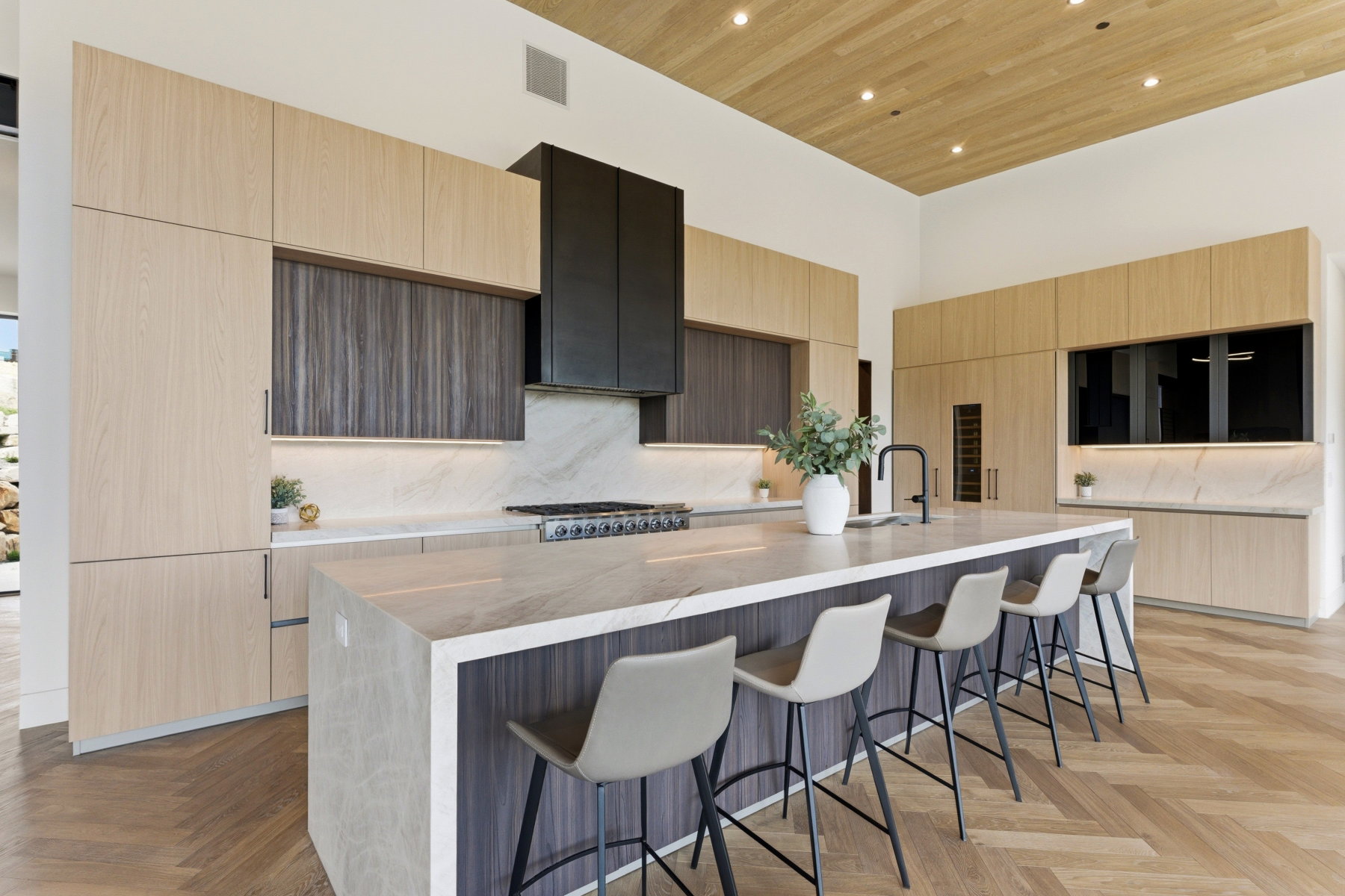 Gourmet kitchen featuring a waterfall island, integrated appliances, and light wood-finish cabinetry