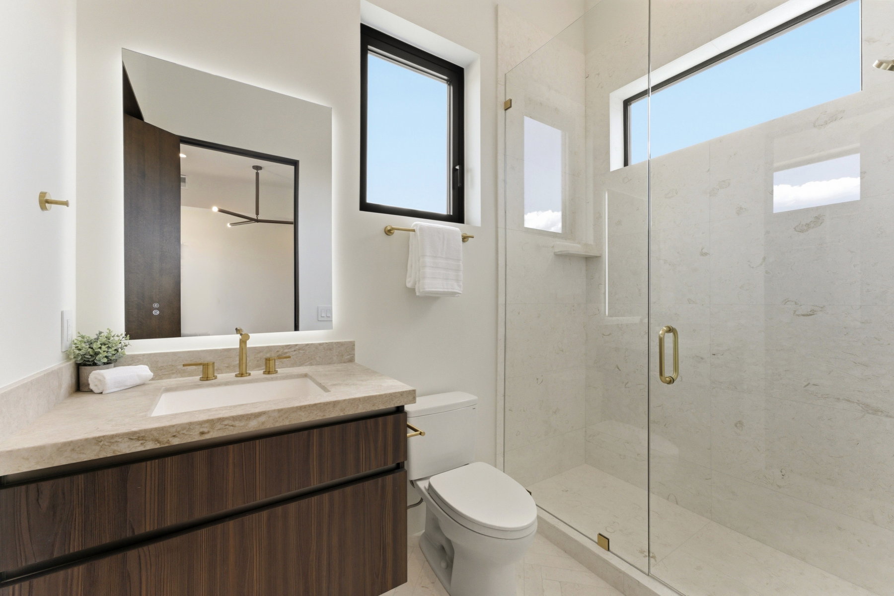Modern bathroom featuring a glass-enclosed shower with tile surround and built-in niche, a floating vanity with a wood-finish base, integrated sink, and an illuminated mirror