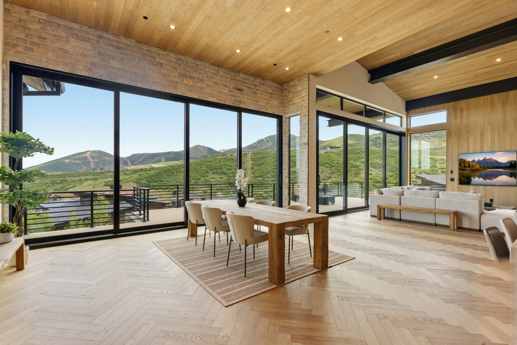 Expansive open-concept living space featuring a vaulted wood-finish ceiling, large format sliding glass doors, herringbone wood-finish flooring, and a stone accent wall