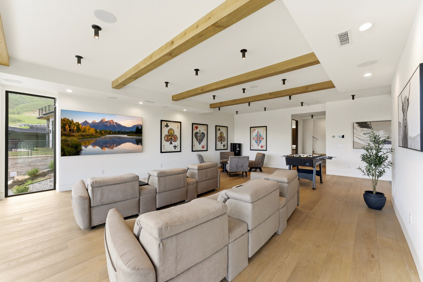Spacious entertainment room featuring exposed wood beams, recessed lighting, wood-finish flooring, a full-height glass panel, and built-in ceiling speakers